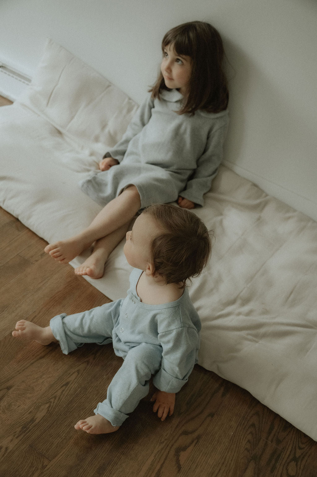 Two children in matching outfits sitting on a bed in a cozy room.