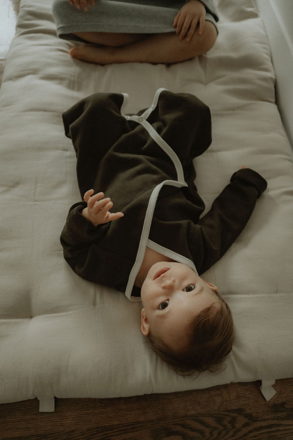 Baby lying on a white mattress with a person partially visible above