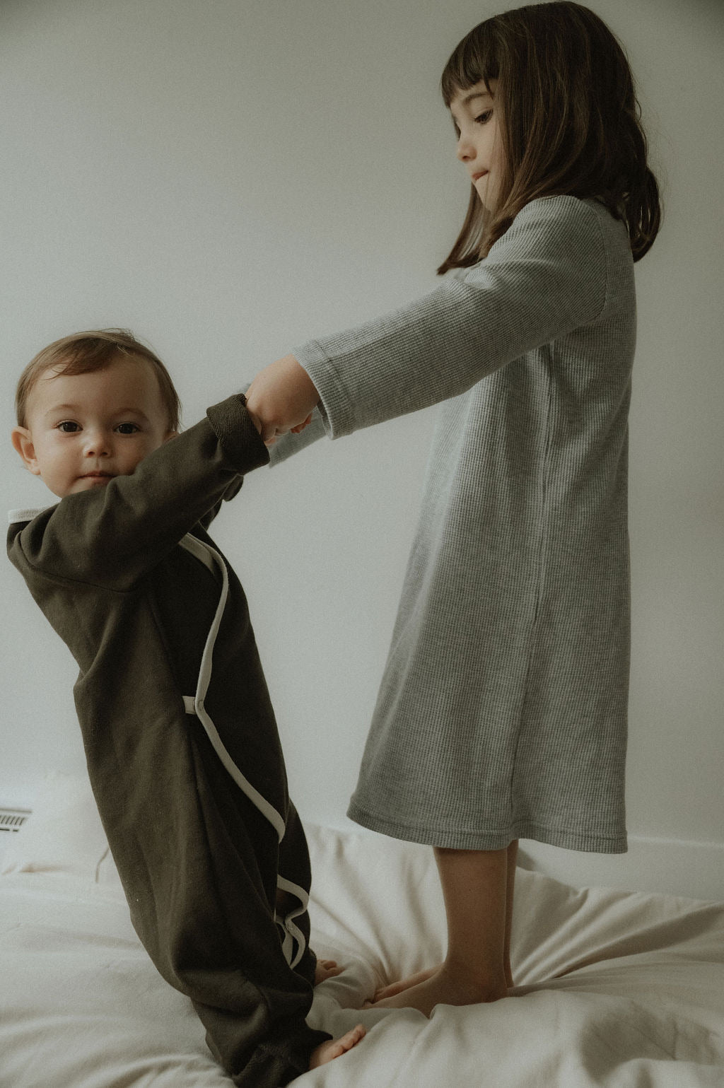 Two children interacting on a bed with a neutral background