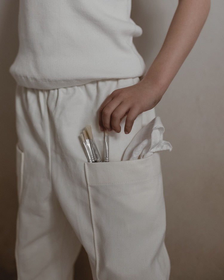 natural twill pant with pocket & paint brushes on girl with white rib top and light beige background