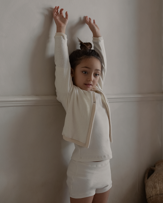 girl with arms up ivory sweater, white top and shorts white backdrop